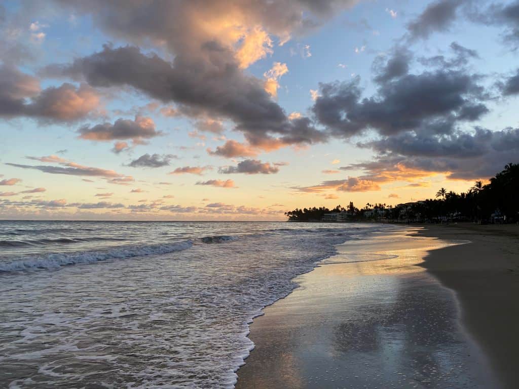 Serene sunset over Cabarete Beach with waves gently lapping the shore under a cloud-filled sky.