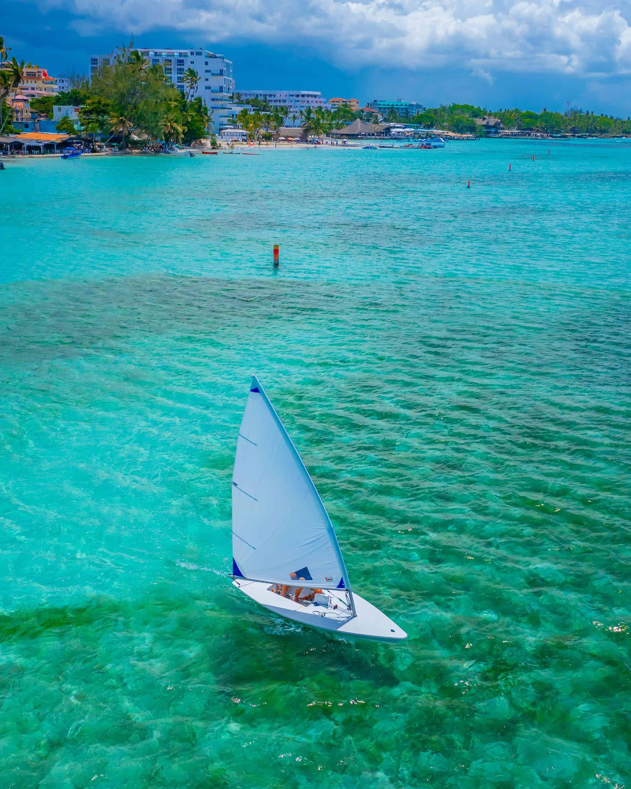 Stunning aerial shot of a sailboat navigating the clear turquoise waters of the Caribbean coast.