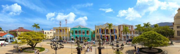 Vibrant Caribbean town square with colonial architecture and lush greenery.